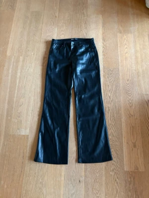 Svarta skinnbyxor från Bershka - Snygga svarta läderbyxor från Bershka med raka ben och klassisk femficksmodell. Byxorna har hög midja och bälteshällor, vilket ger en trendig och stilren look. Perfekta för dig som gillar en modern och edgy stil.