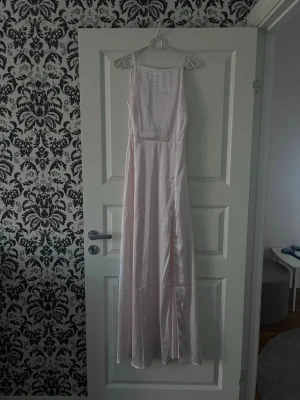 Ljusrosa bal klänning - Ljusrosa långklänning i satinmaterial med smala axelband och v-ringad rygg. Klänningen har en figurnära passform upptill. Använd en gång, inga defekter. Från bubbleroom i storlek 34
