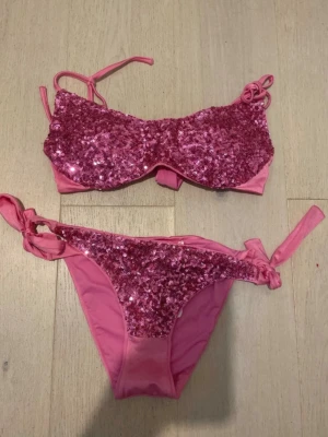 Rosa glitterbikini från Calzedonia - Supersnygg rosa bikini från Calzedonia med glittriga paljetter på både överdel och underdel. Både toppen och trosan har knyt i sidorna för perfekt passform. 
