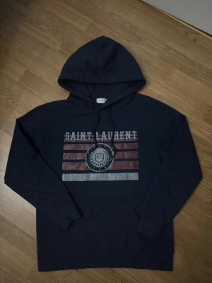 Mörkblå Saint Laurent hoodie - Snygg mörkblå hoodie från Saint Laurent med tryck framtill i vitt och rött.  Storlek 170-175cm. Skriv privat för fler frågor😃
