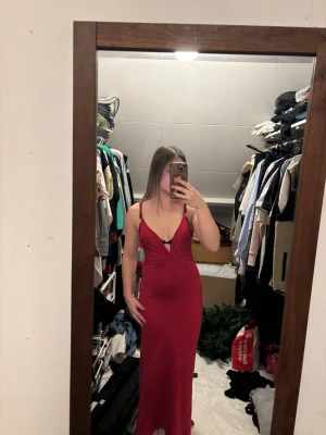 Lång röd klänning med öppen rygg - Snygg långklänning i röd färg med smala axelband och djup v-ringning. Klänningen har en öppen rygg och figurnära passform som framhäver siluetten. Perfekt för dig som vill sticka ut med en elegant look. Aldrig använt 