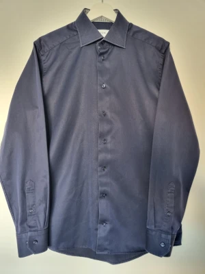 Eton Skjorta Stl 40 - Marinblå skjorta från Eton med mönstrad krage och kroppsnära passform. Den är i mycket bra skick och har inga tecken på användning. Kragomkretsen är 40 cm, vilket motsvarar ungefär en medium/small. Hör av dig om du har fler frågor så svarar jag gladeligen:)