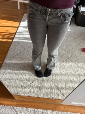 Grå bootcut jeans med fickdetaljer - Säljer ett par grå bootcut jeans med snygga fickdetaljer och kontrastsömmar. Jeansen har låg midja och klassisk femficksmodell. Materialet är stretchigt denim som sitter bekvämt och formar sig efter kroppen. Perfekta för en avslappnad och trendig look. Som ni kan se ser de lite bubbliga ut på bilderna men det syns inte när man har på sig de. Man kan även se lite slitage vid fotändan på byxorna men det syns inte mycket och förstör inte helhetsbilden! De är använda men är i ett bra skick!