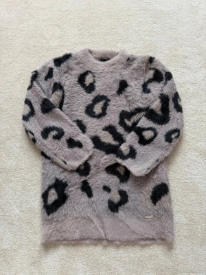 Stickad tröja från GUESS - Supermjuk stickad tröja från Guess i luddigt material med grå bas och svart leopardmönster. Tröjan har rund halsringning och långa ärmar, perfekt för dig som vill sticka ut med en trendig look. Älskar denna tröja!! ⭐️❤️