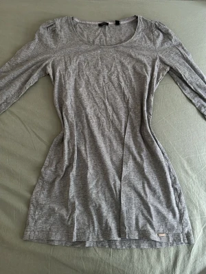 Grå långärmad klänning ESPRIT - En enkel och stilren grå långärmad klänning från ESPRIT. Klänningen har rund halsringning och är tillverkad i mjuk bomullsmix som ger en bekväm passform. Perfekt basplagg att styla med accessoarer eller använda som den är.