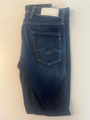 Mörkblå jeans från Replay - Snygga mörkblå jeans från Replay med klassisk femficksmodell och kontrastsömmar. Jeansen har en diskret tvättad look och detaljer som logotyp på fickan och bakficka med unik söm. Tillverkade i mjuk denim med stretch för extra komfort. Liten slitning under gylfen men ej hål! Nästan nya!