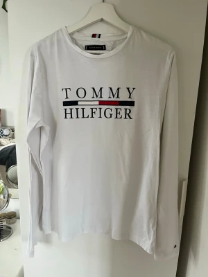 Vit långärmad Tommy Hilfiger - Vit långärmad topp från Tommy Hilfiger med klassisk logga tryckt framtill.