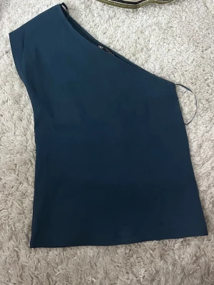 Mörkblå oneshoulder topp från Zara - Snygg mörkblå oneshoulder topp från Zara. Enkel och stilren design med asymmetrisk axel och mjukt material. Perfekt att matcha med jeans eller kjol för en trendig look.