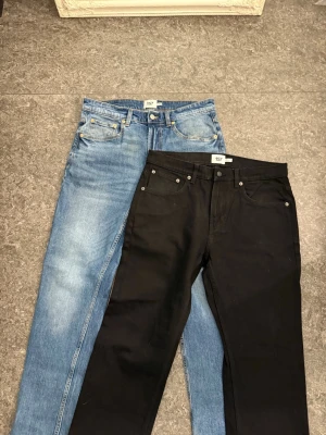 Två par jeans från 157, blå & svarta - Säljer två par klassiska jeans från 157, ett par i ljusblå denim och ett par i svart. Båda har raka ben, fem fickor och knappgylf. Perfekta basjeans i bomull som funkar till allt.