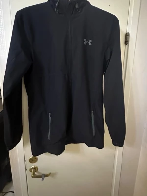  Under Armour -  Under Armour med dragkedja framtill och två fickor med dragkedja. Diskret logga på bröstet och huva baktill. Tillverkad i ett mjukt och bekvämt material, perfekt för chill eller träning.