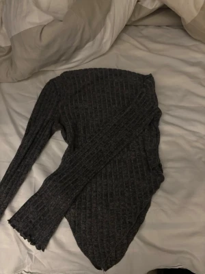 Mörkgrå ribbstickad tröja - Mysig mörkgrå ribbstickad tröja med lång ärm och figurnära passform. Tröjan har en enkel design med diskreta vertikala ränder och rund hals. Perfekt för lager-på-lager och passar till det mesta.