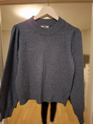 Blå stickad tröja från JDY - Mysig blå stickad tröja från JDY med puffärmar och ribbade muddar vid ärmslut och nederkant. Tröjan har en hög, rund halsringning och är tillverkad i ett mjukt material som passar perfekt för kyligare dagar.