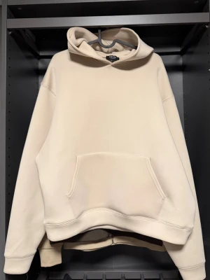 Beige oversized hoodie från MAN - Säljer en beige oversized hoodie från MAN med stor känguruficka framtill och klassisk huva. Hoodien har en clean look utan tryck och är gjord i mjukt bomullsmaterial (scuba). Perfekt för dig som gillar en enkel och avslappnad stil. 