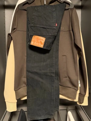 Svarta Levi's jeans raka ben - Säljer ett par svarta jeans från Levi's med klassisk femficksmodell och raka ben. Jeansen har en brun läderpatch bak i midjan och den ikoniska röda Levi's-taggen på bakfickan. Tillverkade i kraftig denim, perfekta för en avslappnad streetstil. Storlek : W28 L32