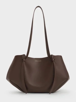 Brun väska från Charles & Keith - Snygg brun väska i slätt konstläder från Charles & Keith. Väskan har en modern, rymlig design med långa axelband och dekorativa knutar på sidorna. Medföljer en matchande necessär med guldfärgad dragkedja. Perfekt för dig som vill ha både stil och funktion. Helt oanvänd och ny🤎