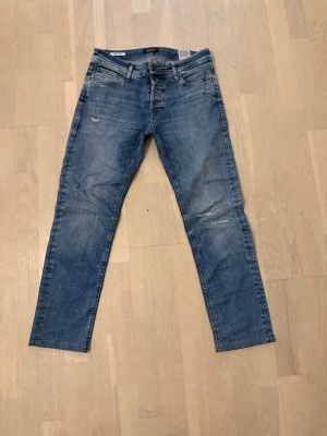 Slim fit jeans från Jack & Jones - Snygga blå slim fit jeans från Jack & Jones, modell Glenn. Jeansen har en klassisk femficksdesign, lätt slitna detaljer och normal midja. Tillverkade i denim med en skön stretch för extra komfort. Perfekta för en avslappnad och trendig look. Förkortade de är egentligen w32/l34 men förkortade till 32/32 