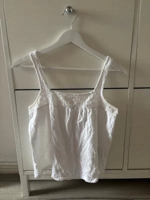 Vit linnetopp med spetsdetaljer - Söt vit linnetopp med breda axelband och fina spetsdetaljer upptill. Toppen är ärmlös och har en luftig passform, perfekt för varma dagar. Enkel att matcha med jeans eller kjol för en fräsch look.💕