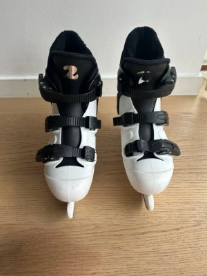 Svarta och vita skridskor R2 - Säljer ett par svarta och vita skridskor från R2 med tre justerbara spännen för perfekt passform. Skridskorna har en robust plastkonstruktion och bekväm innersko i textil. Perfekta för isaktiviteter och träning. Har några små skråmor vilket dj kan se på de två sista sidorna.