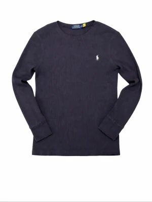 Mörkblå långärmad tröja Polo Ralph Lauren - Mörkblå långärmad tröja från Polo Ralph Lauren med rund halsringning och diskret broderad logga på bröstet. Tröjan är ribbstickad och har en klassisk, stilren design som passar perfekt till jeans eller chinos.