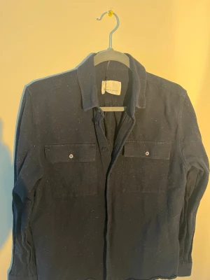 Mörkblå overshirt från Samsøe Samsøe - Snygg mörkblå overshirt från Samsøe Samsøe med diskreta vita prickar. Jackan har två stora bröstfickor med knappar och klassisk krage. Materialet känns som bomull och passformen är normal. Perfekt att slänga på över en t-shirt. 