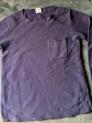 Mörkblå finstickad tröja från Ljung - Tröja från Ljung med rund halsringning och en liten bröstficka. Lite sliten i halsen men knappt märkbart. Snygg till jeans. 100 % bomull. 