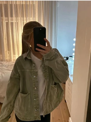 Grön jeansjacka från Zara - Stilren grön jeansjacka från Zara med oversized passform, stora framfickor och klassisk krage. Jackan har knäppning framtill och är tillverkad i mjukt jeansmaterial. Perfekt för en avslappnad och trendig look.