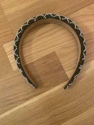 Svart diadem med pärlor - Snyggt svart diadem med pärlbroderi i rutmönster. Diademet är vadderat och dekorerat med små vita pärlor som ger en lyxig känsla. Perfekt accessoar för att lyfta din look med en trendig touch.