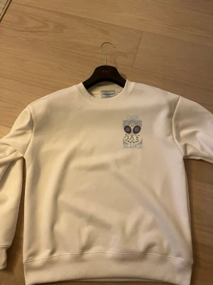 Vit sweatshirt från Casablanca - Säljer en stilren vit sweatshirt från Casablanca med tryck av två tennisrack och texten 'Casa Blanca' på bröstet. Tröjan har rund halsringning och ribbade muddar. Perfekt för dig som gillar sportig och clean stil.sittwr som M