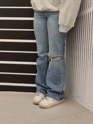 Blå bootcut jeans från Gina tricot - Låg/mid waist Bootcut jeans i ljusblå från Gina tricot, med slitningar och hål på ena knät. Jag är 165cm lång och byxorna når ner till golvet på mig. Lägg gärna ett bud☺️