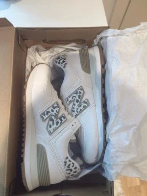 Vita New Balance sneakers med leoparddetaljer - Säljer ett par vita HELT NYA, (fick de igår och det var fel storlek så säljer de ist)New Balance sneakers med snygga leopardmönstrade detaljer på N-loggan och hälen. Skorna har snörning och en beige sula med grå inslag. Strlk 36 dam