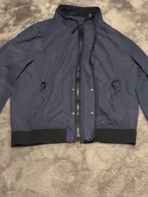 GANT D1 Technical Short Jacket - Säljer en marinblå GANT teknisk bomberjacka i absolut toppskick. Modellen är vind- och vattenavvisande med rejäl tvåvägsdragkedja och klassisk logotyp på ärmen. Inga tecken på användning, rena muddar och tvättlapp kvar.             En helt ny från butik ca 2800kr