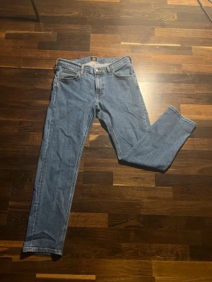 Blå raka jeans med fem fickor - Klassiska blå jeans från Lee. Gylf med dragkedja och knapp. Storlek W31 L30. Passar i stort sätt till allt. Säljer jeansen pga att jag växt hur dom!
