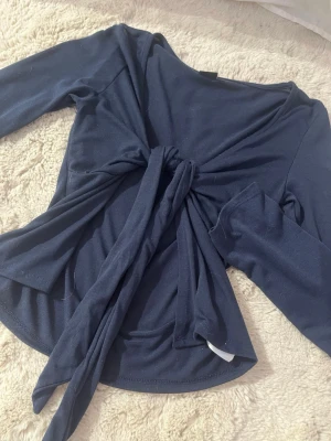 Mörkblå långärmad topp med knyt - Trendig mörkblå långärmad topp med snygg knytning framtill som ger en cool twist på outfiten. Tillverkad i mjukt material som känns skönt mot huden. Perfekt att styla med både jeans och kjol för en avslappnad men ändå chic look.