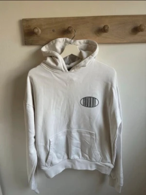 Vit hoodie från Coach Ivy - Vit hoodie med svart tryck framtill och texten 'coach ivy sthlm, sweden' på ryggen. Klassisk känguruficka och huva. Tillverkad i mjukt bomullsmaterial, perfekt för en avslappnad och trendig look. Kanonkvalitet.