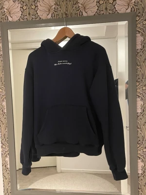 Mörkblå Notre Succès hoodie - Mörkblå hoodie från Notre Succès med vit text och tryck både fram och bak. Klassisk känguruficka och stor huva. Oversized passform och ribbade muddar. Perfekt för en avslappnad och trendig streetwear-look. Inte använd 1 ända gång bara tvättad 1 gång.