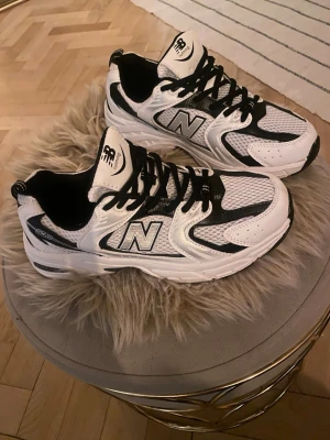 New Balance 530 vita och svarta sneakers  - Snygga New Balance 530 sneakers i vitt och svart med mesh och syntetmaterial. Klassisk siluett med svart N-logga på sidan. Perfekta för en sportig och trendig look. Storlek 39 men  mer slm en 38.