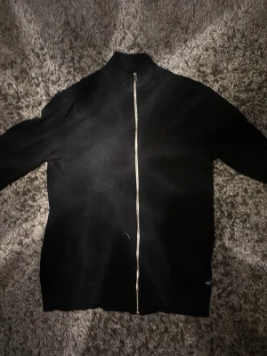 Svart ziptröja från Jack & Jones - Snygg svart ziptröja från Jack & Jones med hel dragkedja framtill och hög krage. Tröjan har en clean look utan synliga loggor på framsidan och är perfekt för lager på lager. Tillverkad i mjukt material som känns skönt mot huden.