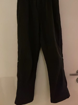 Svarta täckbyxor från Everest - Svarta täckbyxor från Everest med raka ben och reflexdetaljer vid knäna och bensluten. Perfekta för kalla dagar och utomhusaktiviteter. Byxorna har elastisk midja och är tillverkade i ett slitstarkt material som står emot väta och kyla.