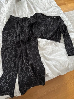 Svart bodyset med silvriga mönster - Säljer ett svart set med långärmad topp och matchande byxor. Båda delar har glittrande linjemönster som ger en cool och modern look.😍🩶