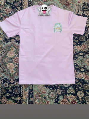 Ljusrosa t-shirt med tryck från Casablanca - Ljusrosa t-shirt från Casablanca med färgglatt tryck av en solig innergård och gröna blad på ryggen samt mindre tryck på bröstet. Klassisk passform och korta ärmar. Perfekt för dig som gillar unika motiv och mjuka färger.Samma dag du köper samma dag jag fraktar 