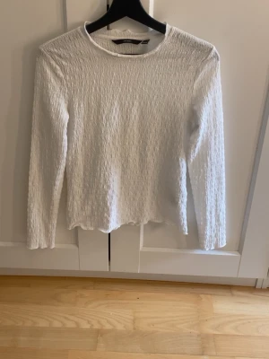 Vit långärmad topp  - Säljer en vit långärmad topp från med crinkle-effekt i materialet. Toppen har rund halsringning och en lätt vågig kant nedtill. Perfekt att styla med jeans eller kjol för en enkel och fräsch look.