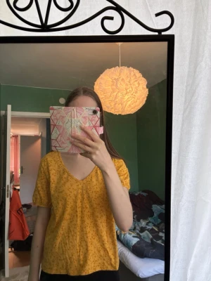 Gul blommig t-shirt med v-ringning - Gul t-shirt från KappAhl med små blommor och v-ringad hals. Kortärmad modell i mjuk bomull, perfekt för en avslappnad stil. Snygg och bekväm med en ljus färgton.