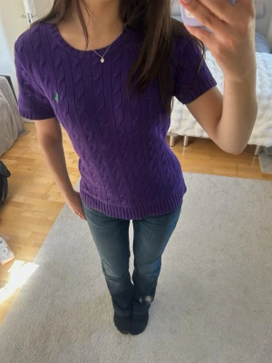 Lila Polo Ralph Lauren kabelstickad tröja nyskick! (Passar S/M) - Säljer en klassisk kortärmad kabelstickad tröja från Ralph Lauren i en lila färg med grön logga. Nyskick, inga defekter eller noppor. Storlek: Står L i lappen, men är liten i storleken (passar perfekt som en S om man vill ha den lite luftig, eller en M för en mer tight passform). Jag är S och den sitter lite luftigt på mig. Hör av dig vid frågor eller för fler bilder! 
