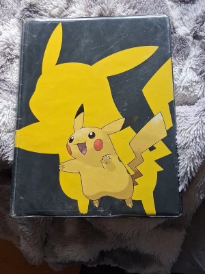 Pokémon pärm med Pikachu-motiv - Säljer en Pokémon pärm från Ultra PRO med stort Pikachu-motiv på framsidan och Pokémon Trading Card Game-logga på baksidan. Pärmen är svart och gul, perfekt för att samla och organisera Pokémonkort. 10 sidor
