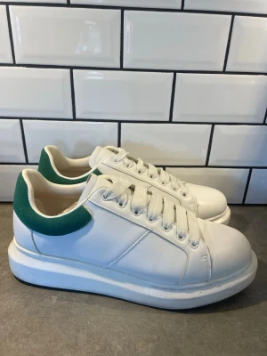 Platform sneakers 45 - Stilrena vita sneakers med tjock sula och grön detalj vid hälen. Skorna har klassisk snörning och är tillverkade i slätt läderliknande material. Perfekta för en clean och modern look. Märke: Loyalty and faith. Storlek:45