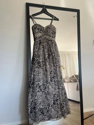 Bal/ festklänning med leopardmönster - Snygg långklänning med leopardmönster i svart, grått och vitt. Klänningen har smala axelband eller så kan man välja att ta bort dom. Markerad byst med lätt drapering framtill och resår i ryggen. 