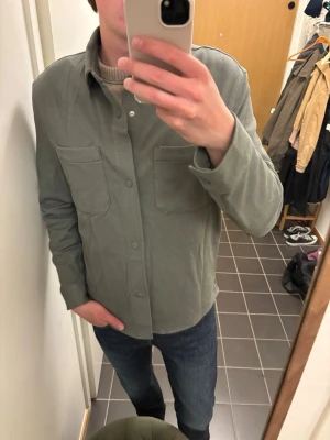 Grön overshirt från Zara - Snygg grön overshirt från Zara med två stora bröstfickor och knäppning framtill. Overshirten har en rak passform och är tillverkad i ett mjukt tyg som känns bekvämt. Perfekt att bära över en t-shirt eller tröja för en avslappnad look.