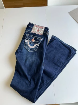 Mörkblå True Religion jeans med rosa detaljer - Jättefina mörkblåa bootcut jeans från true religion. I storlek W25, med rosa detaljer. Nypris 2500, jättesvåra att hitta då dom inte säljas nånstans typ.