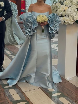 Ljusblå långklänning med volangärmar - Elegant ljusblå långklänning i satin och stora volangärmar formade som blommor. Klänningen har en figurnära passform upptill och har utsvängd kjol med släp. Klänningen har inbyggda knappar för både capen och släpet så att man kan få 3 looks🩵använts endast en gång på bröllop. Köptes för 9000 kr. Storlek 32/34. Säljs snabbt