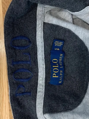 Grå långärmad tröja Polo Ralph Lauren - Snygg grå långärmad tröja från Polo Ralph Lauren med blå broderad logga på bröstet. Tröjan har rund halsringning och är tillverkad i mjukt material som passar perfekt till jeans eller chinos.